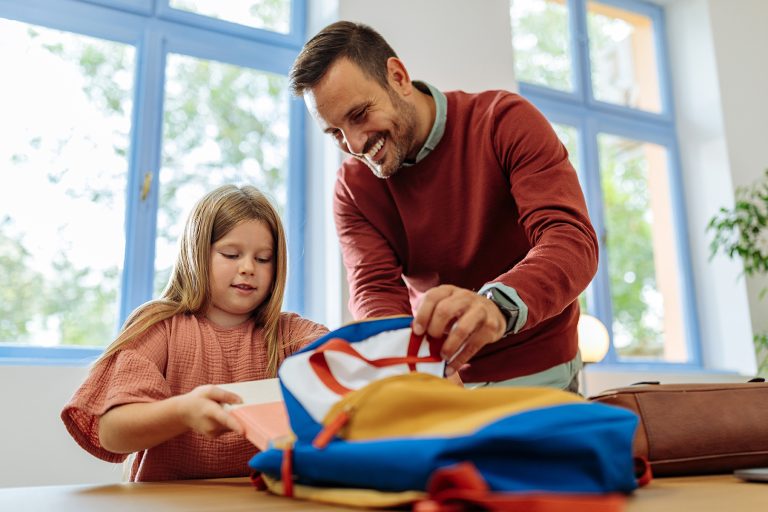 Father and his daughter are putting books in her backpack